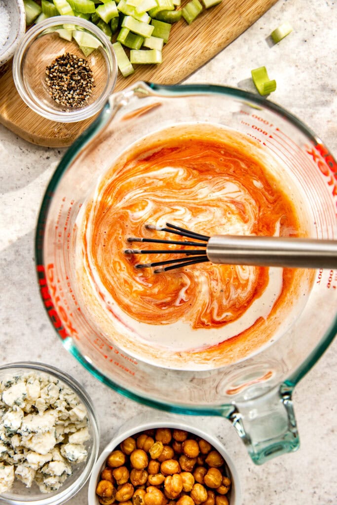 Overhead view of creamy dressing being whisked in a large glass measuring bowl. 