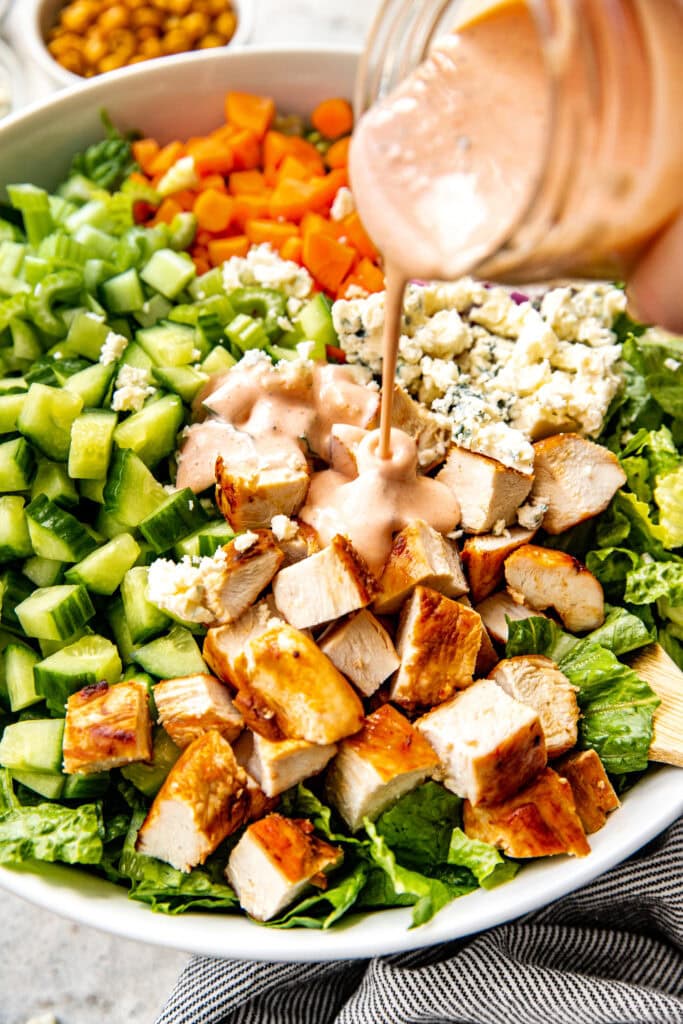 Close up view of creamy dressing being poured over chopped ingredients for buffalo chicken salad. 