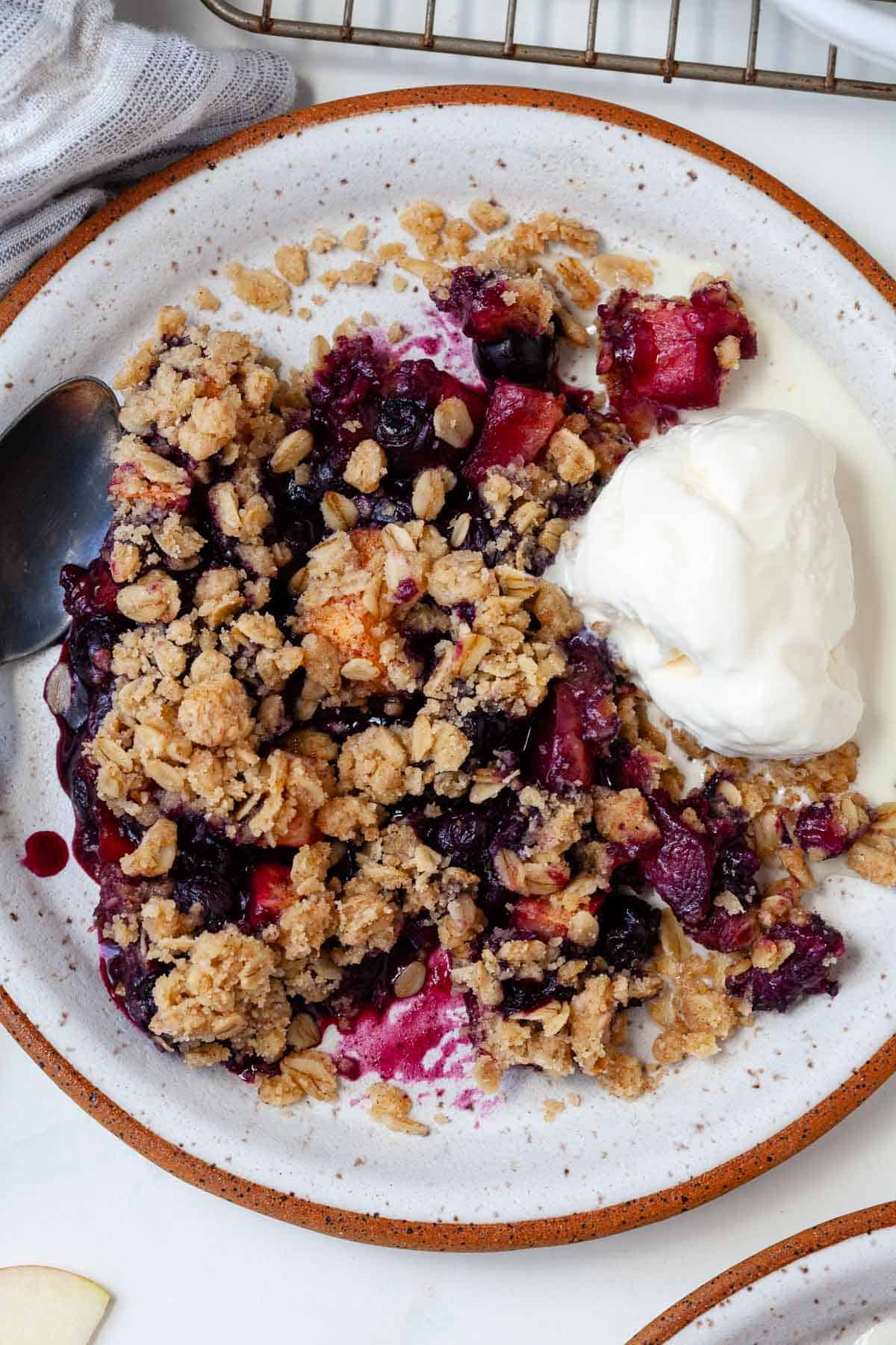 White speckled plate with blueberry apple crisp and scoop of vanilla ice cream.