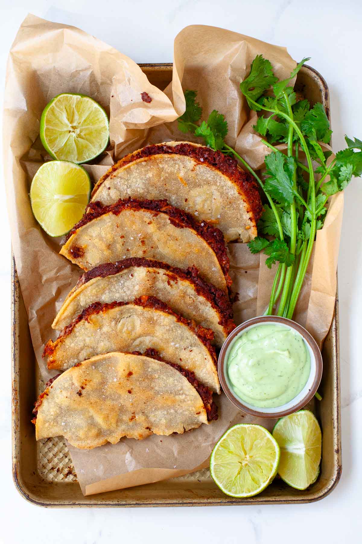 black bean tacos on parchment lined baking sheet with fresh cilantro, lime, and avocado lime crema